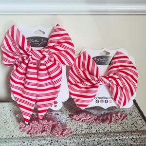 May include: Two red and white striped hair bows and several smaller matching bows are displayed on white cardstock. The bows are arranged on a textured surface. The bows are labeled with the text "by Yoella Zim".