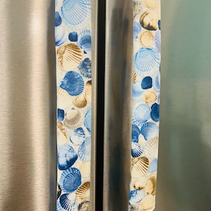May include: Two blue and brown fabric refrigerator handle covers with a seashell pattern.