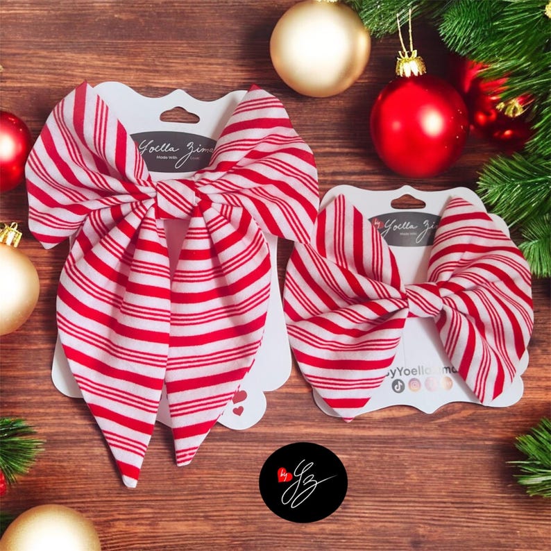 May include: Two red and white striped fabric bows on white cardstock, with the text "Yoella Zi". The bows are displayed on a wooden surface, with Christmas ornaments and greenery in the background. A black circle with a signature is in the bottom.