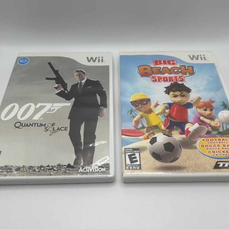 K&ouml;nnte beinhalten: Zwei Wii-Videospielh&uuml;llen. Eine zeigt einen Mann im Anzug mit einer Waffe, mit dem Text "007 Quantum of Solace". Die andere H&uuml;lle zeigt Zeichentrickfiguren beim Sport mit dem Text "Big Beach Sports."