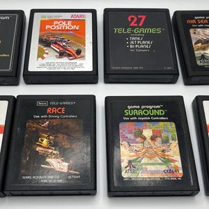Może przedstawiać: Osiem gier na konsolę Atari 2600, w tym Casino, Pole Position, 27 Tele-Games, Air Sea Battle, Vanguard, Race, Surround i Raiders of the Lost Ark. Gry są czarne z srebrnymi etykietami i zawierają tytuły gier oraz opisy.