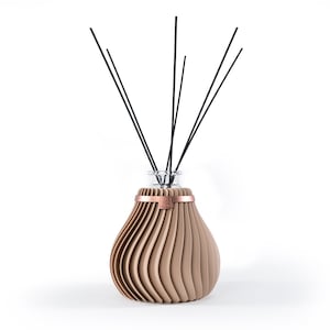 Könnte beinhalten: Eine braune Keramik-Diffuserflasche mit einem kupferfarbenen Band um den Hals. Die Flasche hat ein geripptes Design und ist mit schwarzen Diffusorsticks gefüllt.