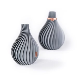 Könnte beinhalten: Zwei graue Keramikvasen mit geripptem Design. Die Vase links hat ein braunes Etikett mit dem Wort "BRISM" darauf. Die Vase rechts hat ein kupferfarbenes Band um den Hals.