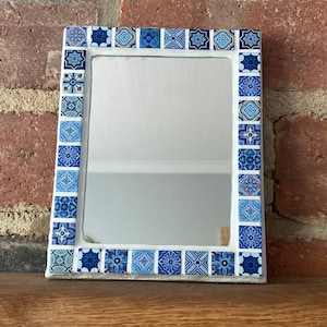 May include: A small rectangular mirror with a white frame decorated with blue and white mosaic tiles.