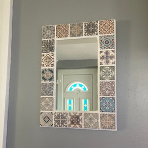 May include: A white framed mirror with a decorative border of colourful patterned tiles. The mirror reflects a white door with a stained glass window.
