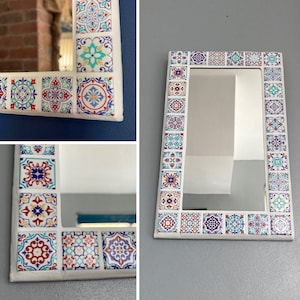 May include: A white rectangular mirror with a decorative border of colourful patterned tiles. The tiles are in shades of blue, red, yellow, and white.