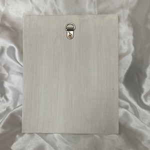 Op de afbeelding: Een witte houten plaquette met een zilveren metalen ophanglus aan de bovenkant.