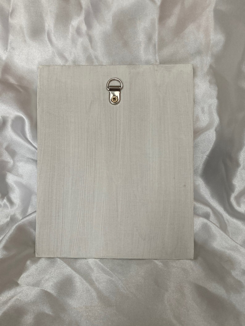 Op de afbeelding: Een witte houten plaquette met een zilveren metalen ophanglus aan de bovenkant.