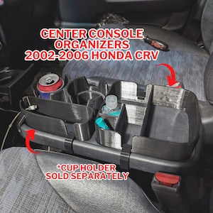 May include: Black plastic center console organizer for a 2002-2006 Honda CRV. The organizer has multiple compartments for storing items like phones, wallets, and drinks. *Cup holder sold separately.*