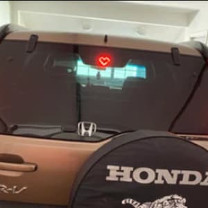 以下が含まれることがあります： リアウィンドウに赤いハート型のステッカーが貼られた、茶色のホンダCR-V。スペアタイヤカバーには「HONDA」の文字が印刷されています。