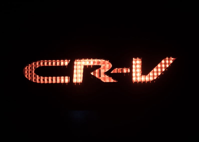 以下が含まれることがあります： グリッド状のライトで照らされた赤い「CR-V」ロゴ