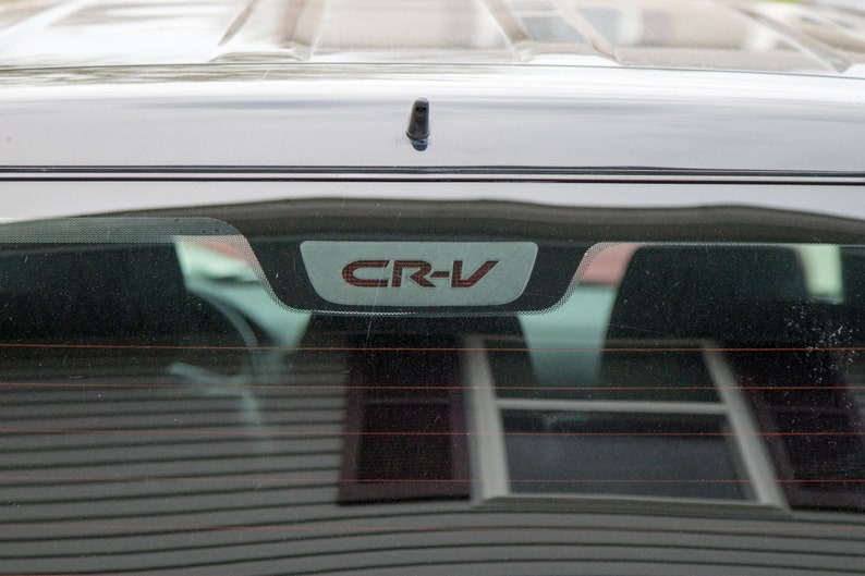 以下が含まれることがあります： リアウィンドウにグレーとレッドの「CR-V」エンブレムが付いたシルバーの車