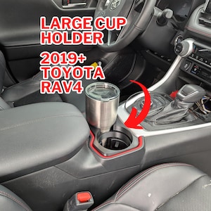 May include: A large cup holder for a 2019+ Toyota RAV4. The image shows a stainless steel tumbler in the cup holder. The cup holder is black with a red trim, and the text "LARGE CUP HOLDER 2019+ TOYOTA RAV4" is displayed in red.
