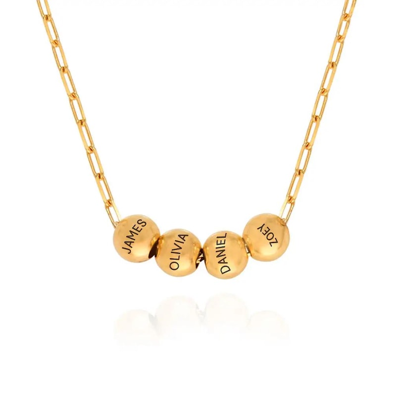 K&ouml;nnte beinhalten: Goldkette mit vier runden Perlen, jede mit einem Namen graviert: James, Olivia, Daniel und Zoey.