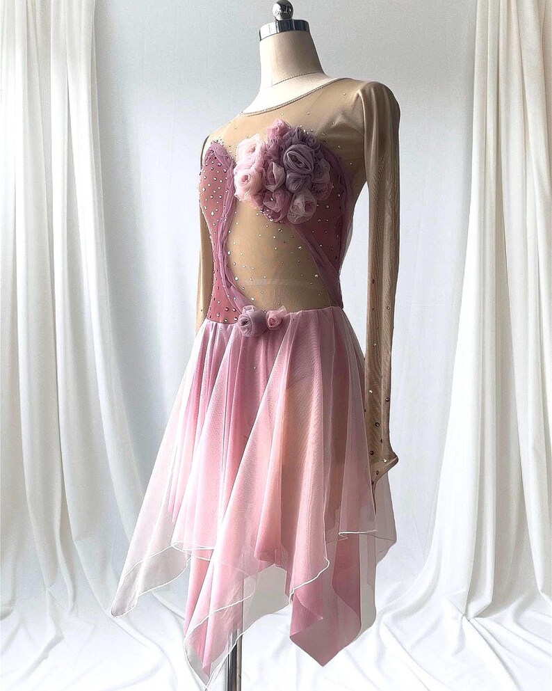 May include: A long-sleeved dance dress featuring a nude mesh bodice with mauve fabric panels, scattered rhinestones, and a large cluster of fabric roses on the chest. The skirt consists of layered, asymmetrical mauve tulle with white trim.