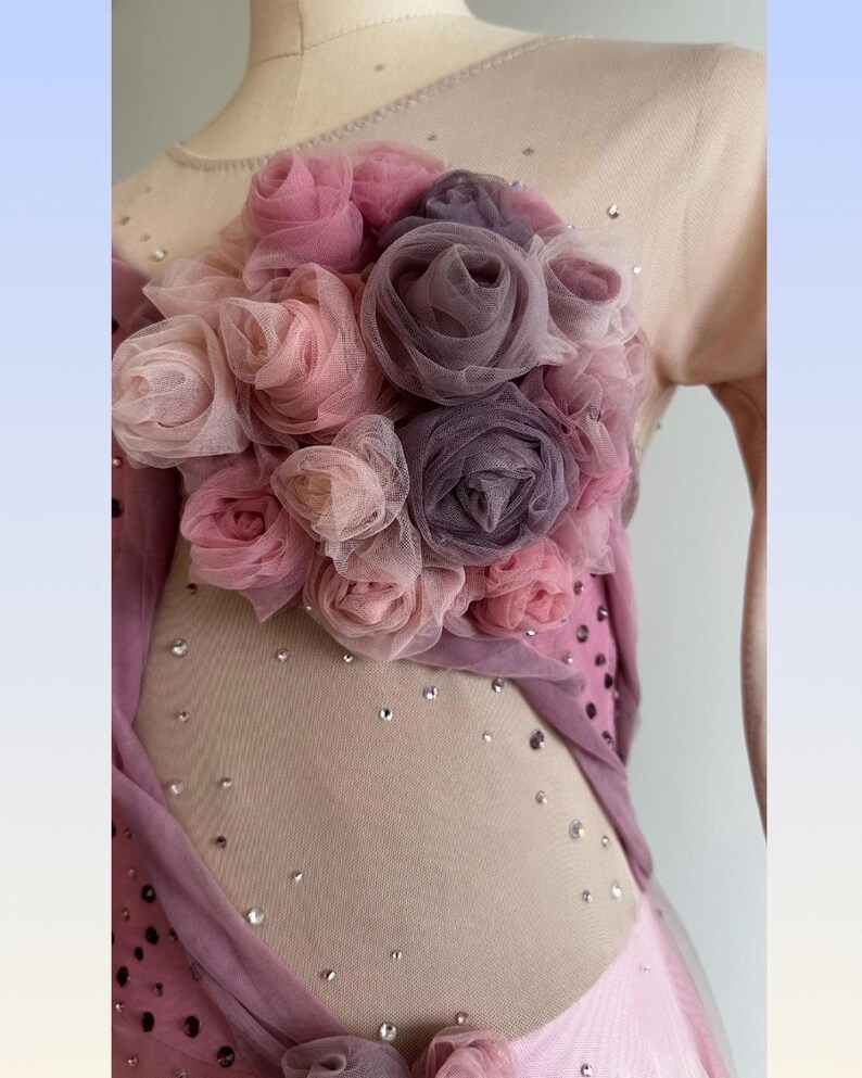 May include: A sleeveless garment featuring a nude-colored mesh bodice adorned with scattered clear crystals and a cluster of layered fabric roses in shades of dusty pink, mauve, and muted purple, with additional fabric draping along the side.