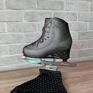 May include: A black ice skate featuring a mesh overlay adorned with small silver rhinestones, paired with a matching black fabric skate cover also decorated with silver rhinestones. The skate has a silver metal blade attached to the base.