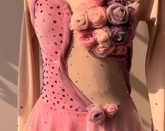 May include: A long-sleeved leotard featuring a nude-colored mesh bodice with pink fabric panels, scattered clear crystals, and a cluster of fabric roses in shades of pink and purple on the chest and waist, paired with a layered pink tulle skirt.
