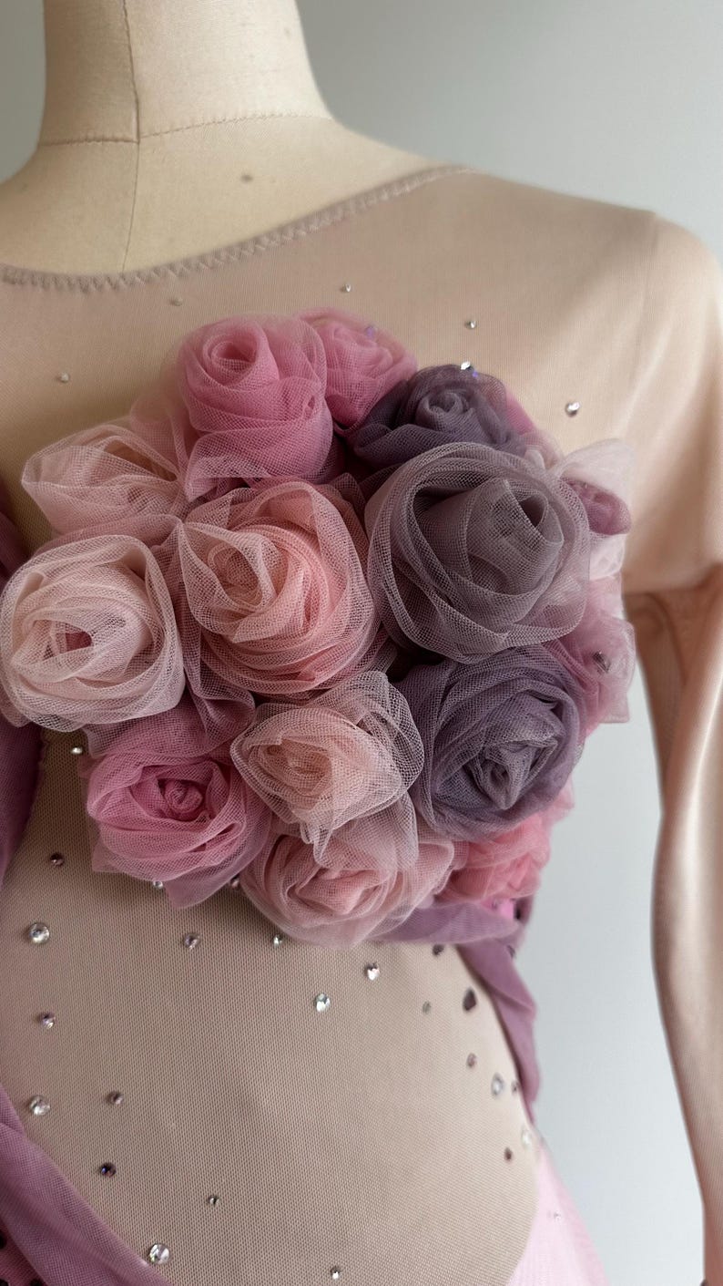 May include: A beige bodice featuring a cluster of layered tulle roses in shades of dusty pink, mauve, and deep plum. The garment is embellished with scattered clear crystals across the sheer fabric, creating a textured floral focal point.