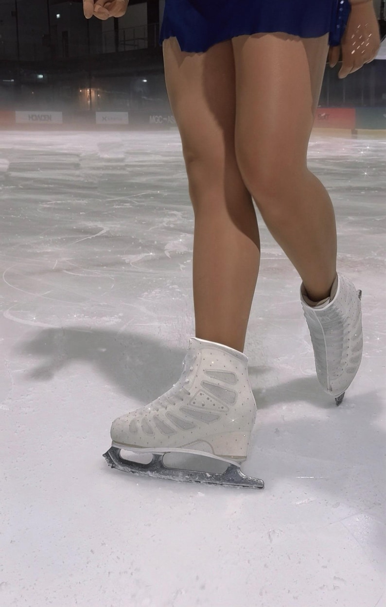 May include: A pair of white figure skates with metallic blades, featuring a lace-up design and subtle sparkling embellishments on the boot exterior, worn on an ice rink surface.