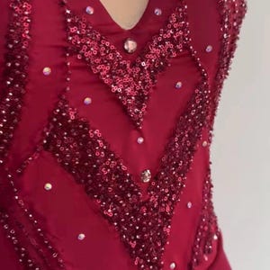 May include: A deep red bodice featuring a sweetheart neckline with a sheer mesh insert. The fabric is heavily embellished with dark red sequins arranged in chevron patterns, accented by scattered clear crystals throughout the front surface.