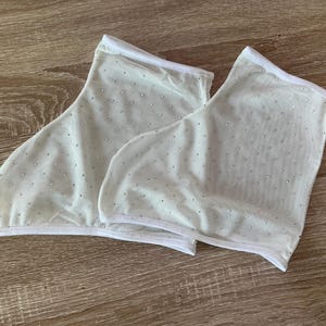 May include: A pair of off-white sheer mesh ankle socks featuring a scattered pattern of small, reflective silver rhinestones throughout the fabric. Each sock is finished with a clean white hem along the top and bottom edges for structure.