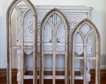 May include: Set of three whitewashed wood arched windowpane wall decor. The windows are different sizes and have a distressed look.