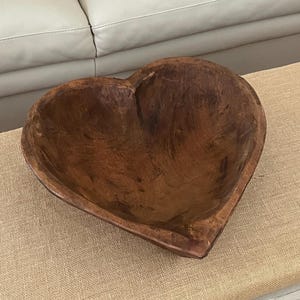 May include: A large, heart-shaped wooden bowl with a dark brown finish. The bowl is made of natural wood and has a rustic, vintage look.