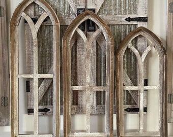 May include: Three rustic wooden arched window frames with a distressed white paint finish. The frames are arranged in a row, with the largest frame on the left and the smallest frame on the right.