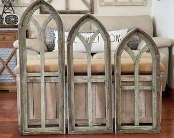 May include: Three rustic wooden arched windowpane wall decor pieces in a distressed green and white finish. The pieces are arranged in a row on a wooden floor.