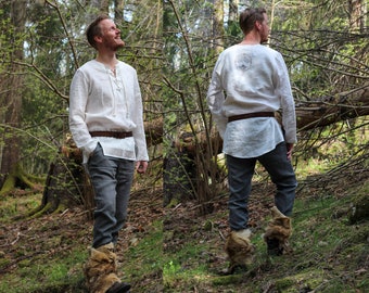 May include: Two people wearing white linen shirts with long sleeves and brown leather belts. The shirts have a simple design and are worn with gray pants. Both people are wearing brown fur-lined boots. The background is a forest setting.