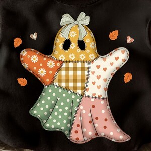 Op de afbeelding: Zwart sweatshirt met een patchwork spookontwerp. Het spook is gemaakt van verschillende stoffen met patronen, waaronder madeliefjes, harten, stippen en ruitjes. Een strik siert het hoofd van het spook, met herfstbladeren en harten verspreid rond het ontwerp.