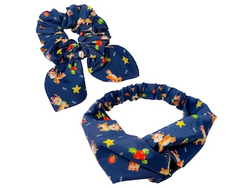 May include: A navy blue scrunchie with a bow and a matching headband. Both are patterned with reindeer, stars, and Christmas ornaments. The scrunchie has a bow, and the headband has a twisted design.