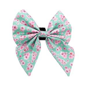 May include: A green bow tie with a pink floral pattern. The bow tie is made of fabric and has a black elastic band.