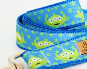 May include: A blue dog leash with a green alien pattern and stars. The leash has a silver clip and a brown tag that says "Bowes' Collars".