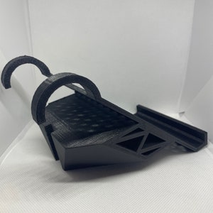 May include: A black 3D printed phone stand with a curved design and a raised platform for holding a phone.