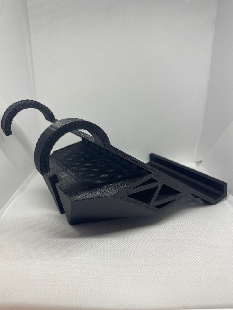 May include: A black 3D printed phone stand with a curved design and a raised platform for holding a phone.