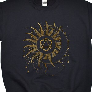 Puede incluir: Sudadera negra con un dise&ntilde;o dorado de sol y luna. El sol tiene rayos puntiagudos y una forma geom&eacute;trica en el centro. La luna tiene forma de media luna. L&iacute;neas punteadas y peque&ntilde;os c&iacute;rculos rodean el sol y la luna.