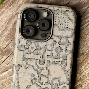 May include: A beige iPhone case featuring a black and white dungeon map design. The case has a raised camera bump with three black camera lenses. The text "Dungeon Atelier" is visible in the bottom right corner of the image.