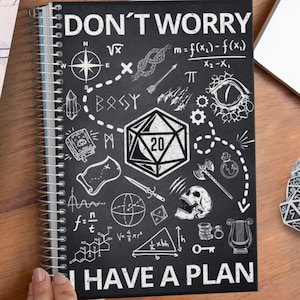Può includere: Un taccuino nero con una rilegatura a spirale bianca. La copertina presenta un'illustrazione in bianco e nero di un dado a 20 facce, un teschio, una bussola e altri simboli. Il testo "DON'T WORRY I HAVE A PLAN" è stampato in bianco sulla copertina.