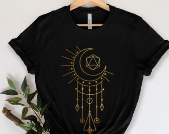 May include: Black t-shirt with a gold design of a crescent moon, a geometric shape, and dangling charms. The design resembles a dreamcatcher.
