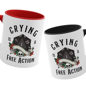 May include: Two white ceramic mugs with black and red accents. Both mugs feature a black and white illustration of a twenty-sided die with the text "Crying is a Free Action".