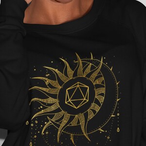 Puede incluir: Sudadera negra con un dise&ntilde;o dorado de sol y luna. El sol presenta una forma geom&eacute;trica en su centro. El dise&ntilde;o est&aacute; detallado con l&iacute;neas y puntos, creando una est&eacute;tica celestial y m&iacute;stica.