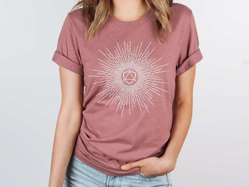 Puede incluir: Una camiseta color malva con un gr&aacute;fico blanco de un sol radiante con un dise&ntilde;o geom&eacute;trico en el centro.
