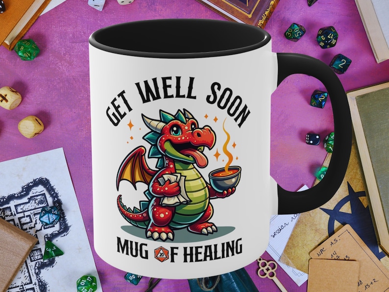 May include: White ceramic mug with a black handle. The mug has a cartoon illustration of a red dragon holding a steaming mug. The text "Get Well Soon Mug of Healing" is printed on the mug.