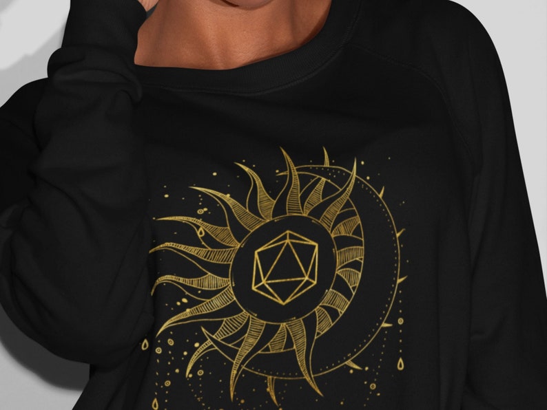 Puede incluir: Sudadera negra con un dise&ntilde;o dorado de sol y luna. El sol presenta una forma geom&eacute;trica en su centro. El dise&ntilde;o est&aacute; detallado con l&iacute;neas y puntos, creando una est&eacute;tica celestial y m&iacute;stica.