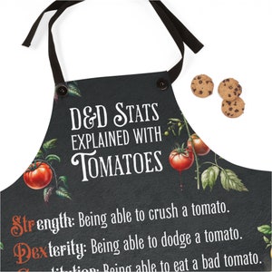 以下が含まれることがあります： 「D&D Stats Explained With Tomatoes」と書かれた白いデザインの黒いエプロン。デザインには、赤いトマトと緑の葉が付いたトマトのつるが含まれています。タイトルの下のテキストには、「Strength: Being able to crush a tomato. Dexterity: Being able to dodge a tomato. Constitution: Being able to eat a bad tomato.」と書いてあります。