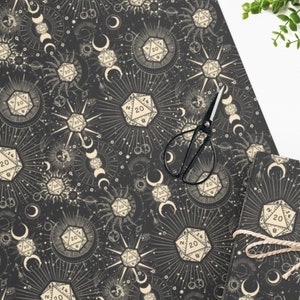May include: Black and white wrapping paper with a repeating pattern of dice, moons, and stars. The dice are 20-sided and have the number 20 on them. The moons are crescent shaped and the stars are small and scattered.
