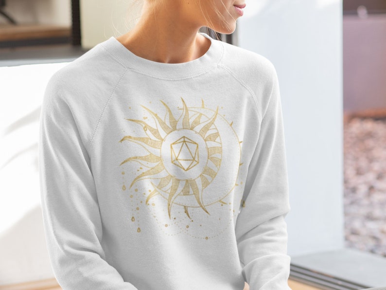 Puede incluir: Sudadera blanca con un dise&ntilde;o dorado de sol y luna con una forma geom&eacute;trica en el centro. El sol tiene rayos detallados y la luna tiene forma de media luna. El dise&ntilde;o tiene un tema celestial.