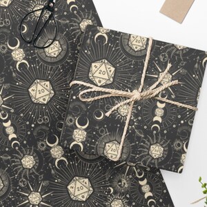 May include: Black and white wrapping paper with a repeating pattern of dice, moons, and suns. The dice are 20-sided and have the number 20 on them. The moons and suns are stylized and have a celestial feel.